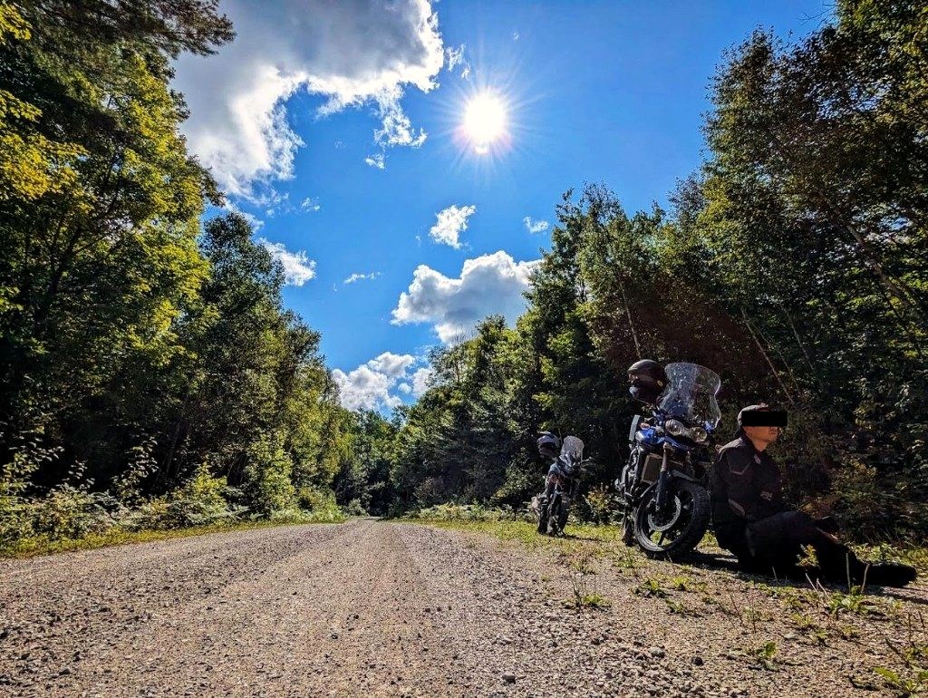 Adventure motorcycles parked on a gravel backroad in an Ontario forest