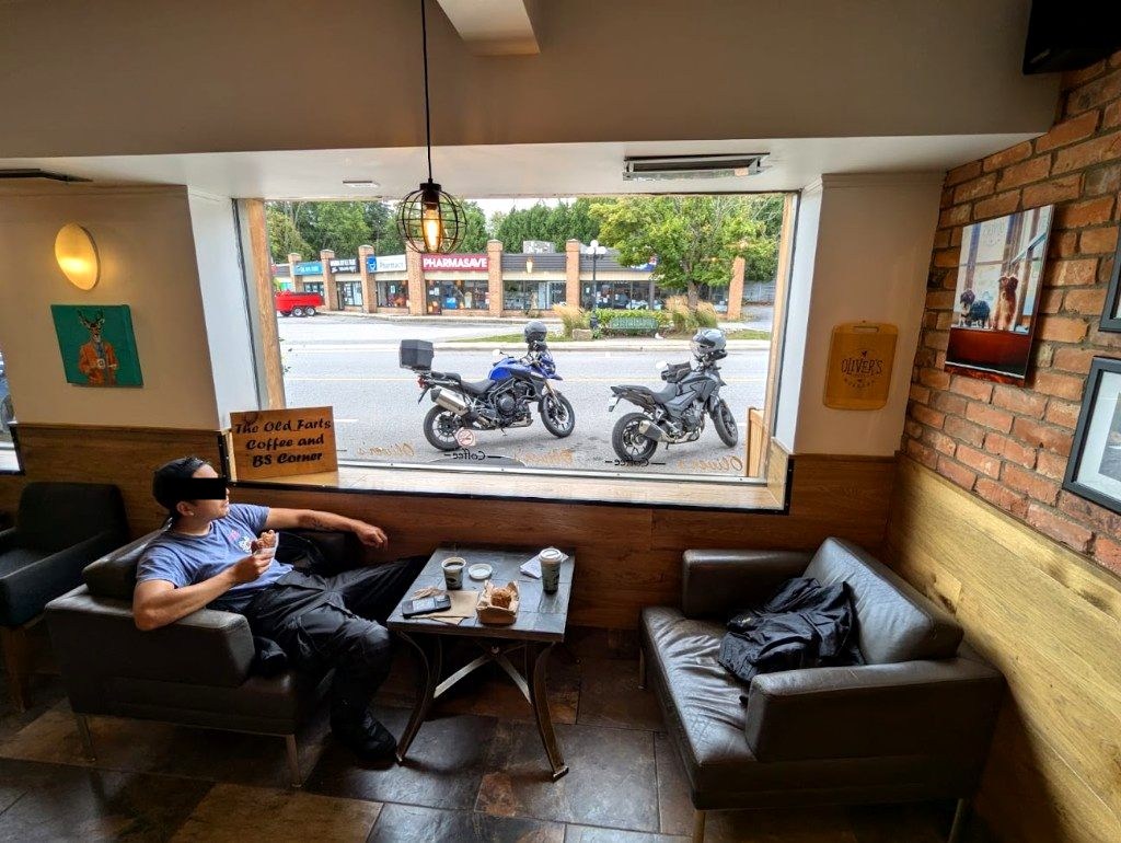 Alex at a cafe with two adventure motorcycles parked outside the window